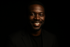 A black men confidently showing his skin face with smile in black background with minimal lighthing on face